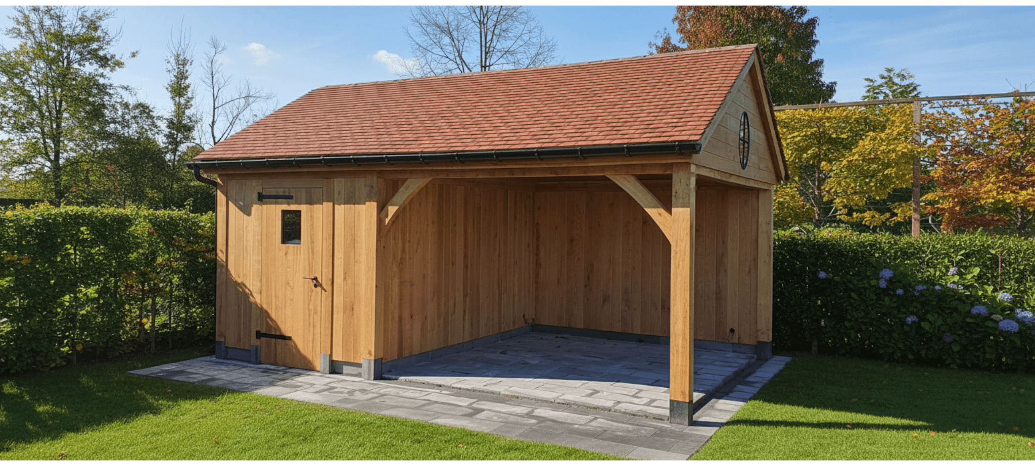 Houten tuinschuur met rood pannendak en open voorkant, omgeven door groen gazon, hagen en bloemen.